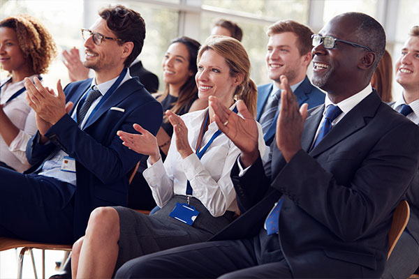 Bilden visar en samling av människor som applåderar under en konferens