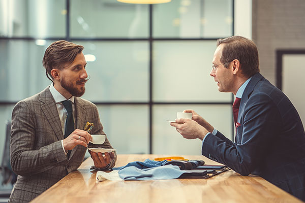 Bilden visar två kostymklädda personer som diskuterar affärer över en kopp kaffe