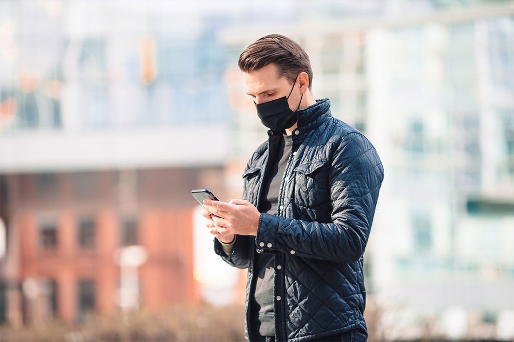 Bilden visar en man med munskydd som tittar på sin telefon under coronapandemin