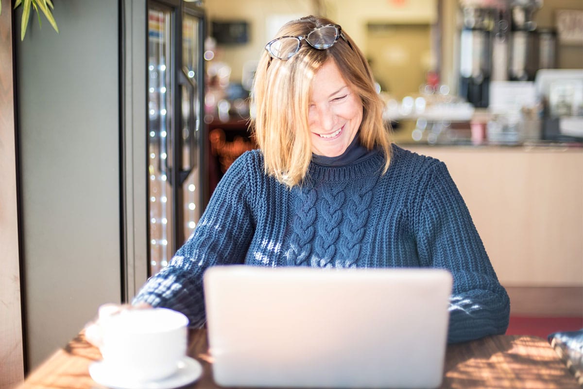 En medelålders kvinna i ett café med bärbar dator
